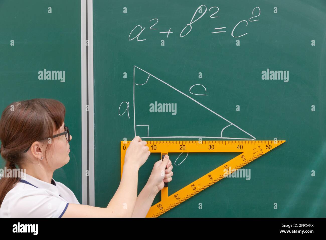 insegnante di scuola giovane donna nella classe al lavagna disegna un triangolo con un righello. ritratto. primo piano Foto Stock