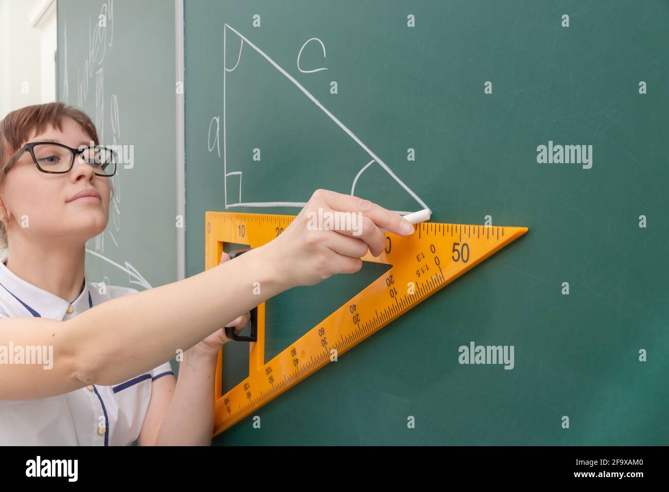insegnante di scuola giovane donna nella classe al lavagna disegna un triangolo con un righello. ritratto. primo piano Foto Stock