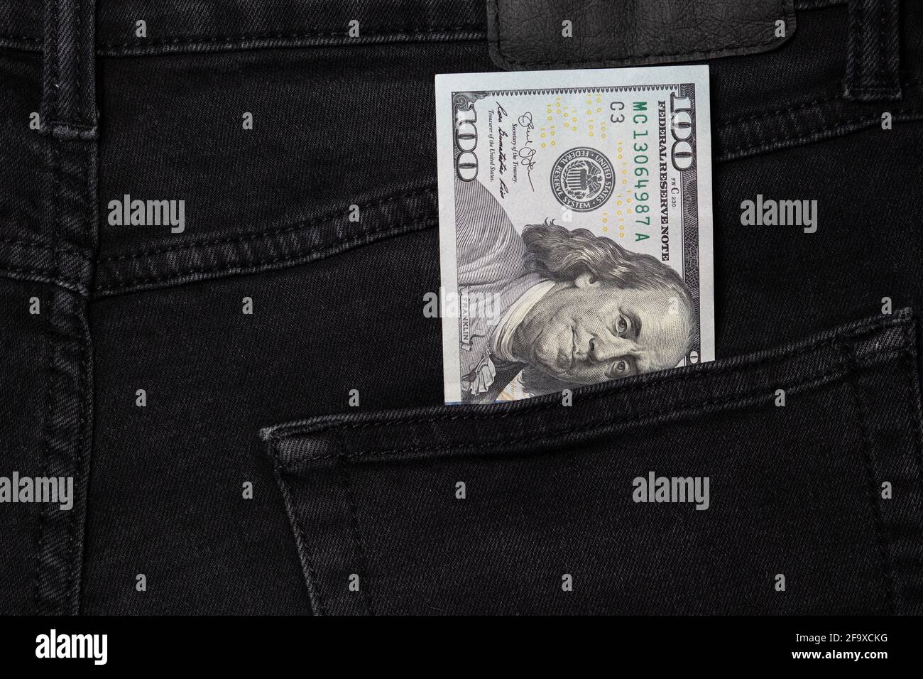 Un conto di cento dollari che si stacca dalla tasca di jeans neri Foto Stock