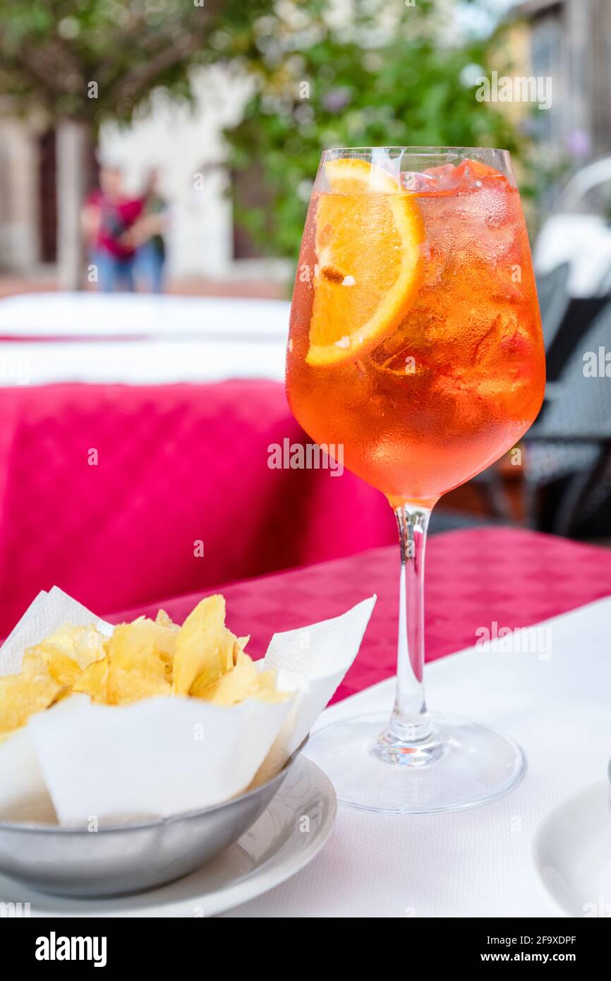 bicchiere di cocktail aperol spritz sul tavolo esterno al sole giorno con ciotola di patatine in primo piano Foto Stock