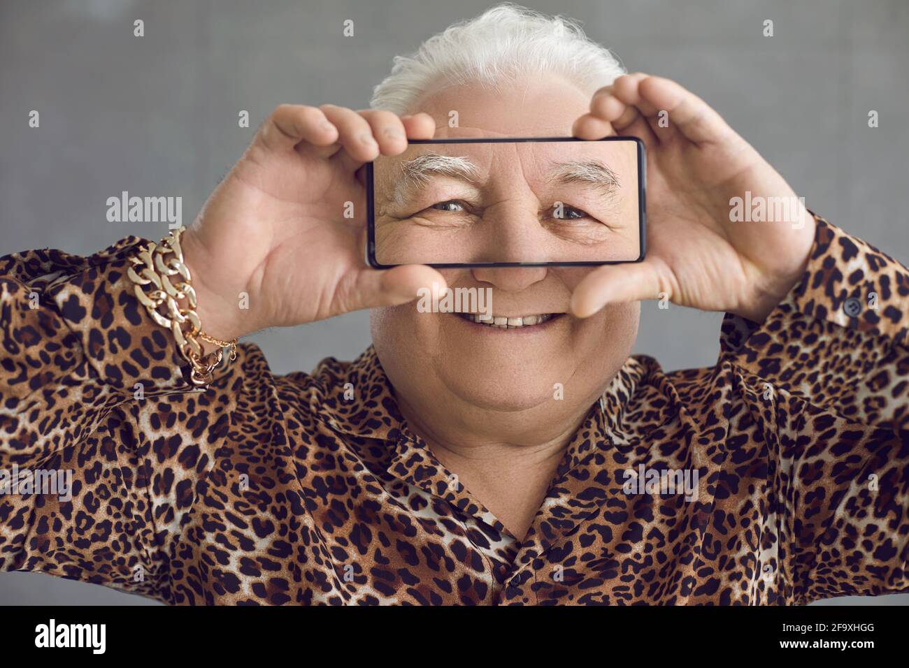 Divertente e ricco Chubby uomo anziano in una camicia leopardo avendo divertimento con il suo telefono cellulare Foto Stock