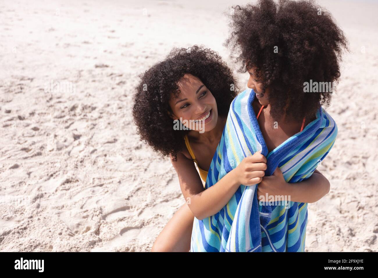 Madre afroamericana e figlia che avvolgono con un asciugamano a. la spiaggia sorridente Foto Stock