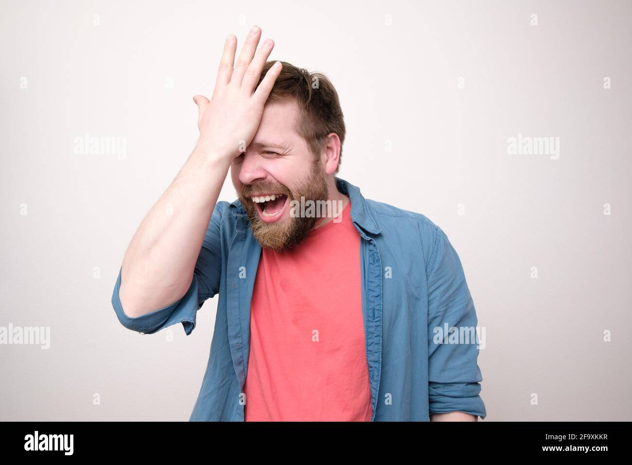 L'uomo allegro e ridente è felice di ricordare qualcosa di importante, di tenere la mano sulla fronte e di gioire. Foto Stock