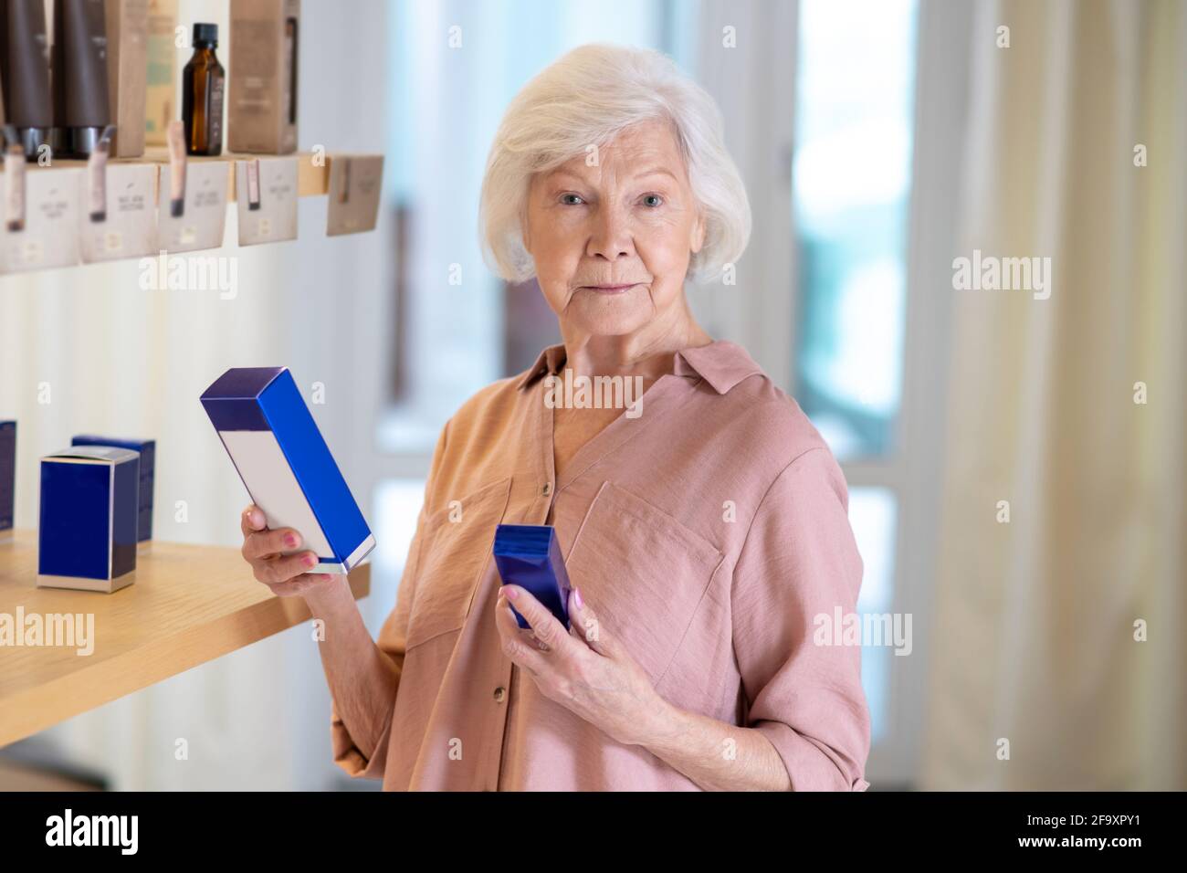Donna dai capelli grigi che sceglie i profumi in una boutique Foto Stock
