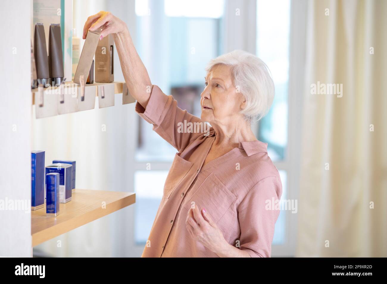 Donna matura dai capelli corti che sceglie i profumi in una boutique Foto Stock