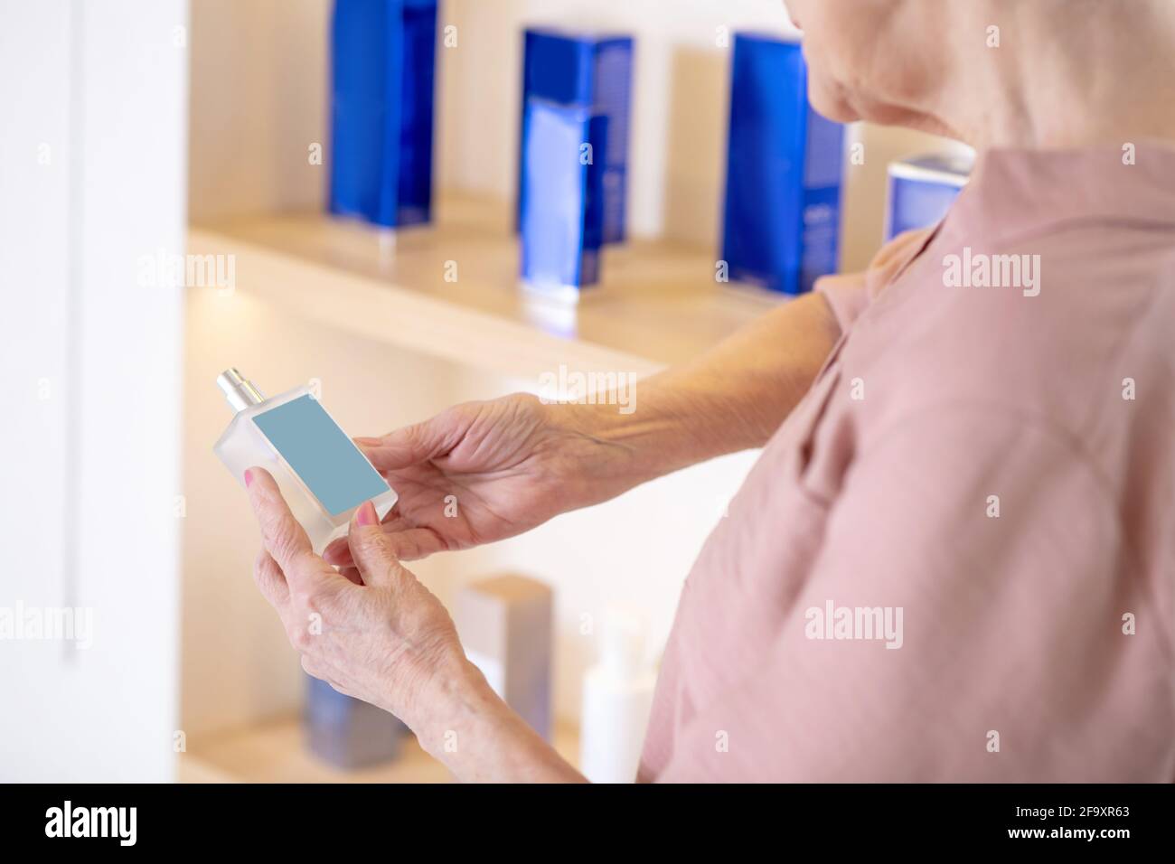 Donna matura dai capelli corti che sceglie i profumi in una boutique Foto Stock