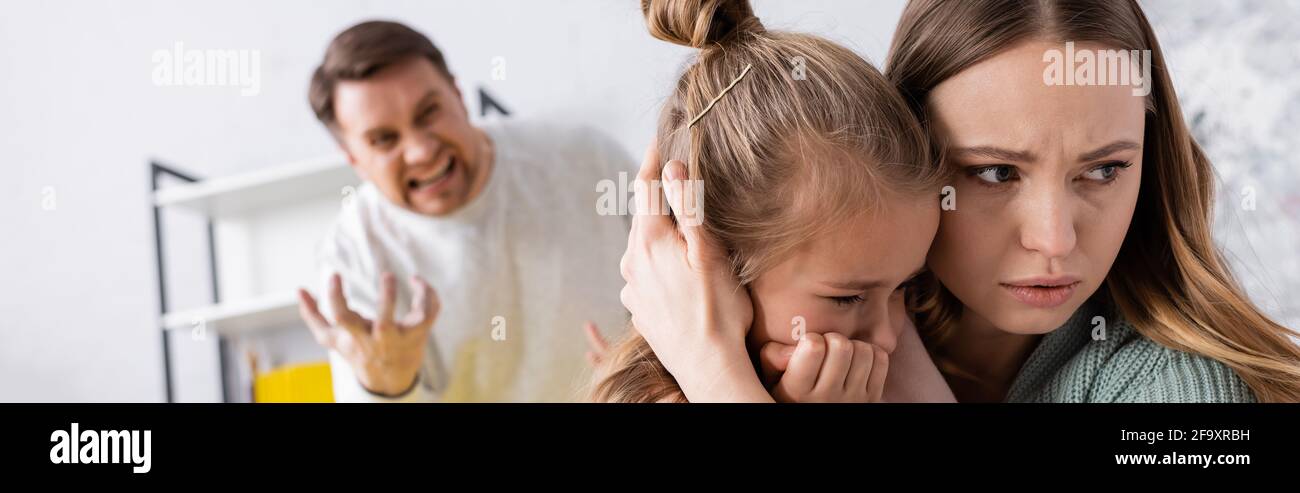 Donna abbracciando bambino vicino urlare padre, bandiera Foto Stock