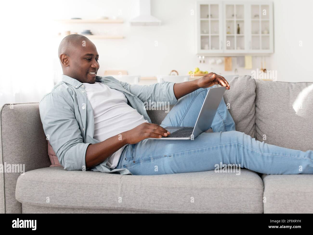 Buon freelance di mezza età che utilizza un computer portatile moderno, avendo lavoro part-time a casa, seduto sul divano Foto Stock