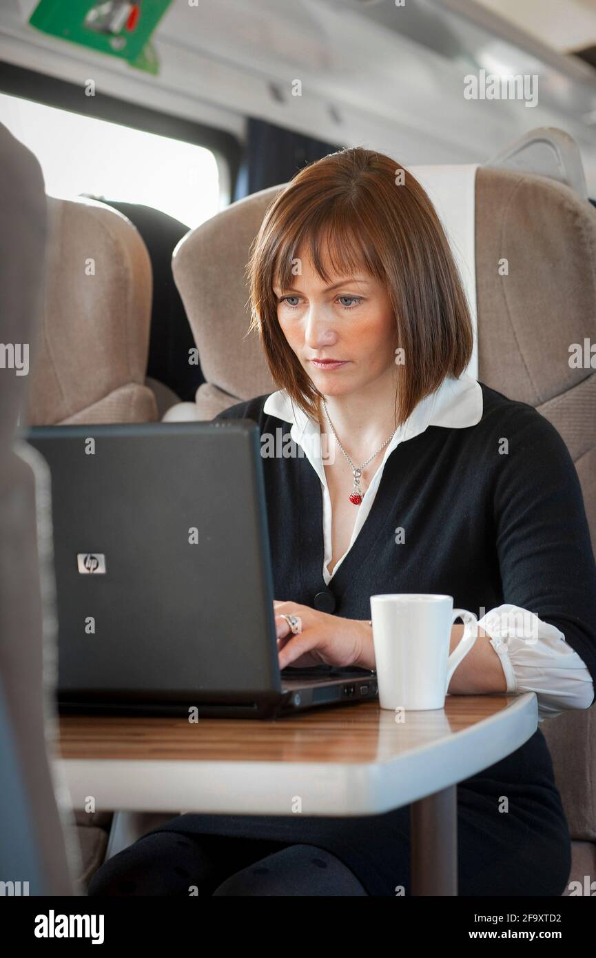 Giovane donna che lavora su un computer portatile mentre viaggia su un treno nel Regno Unito. Foto Stock