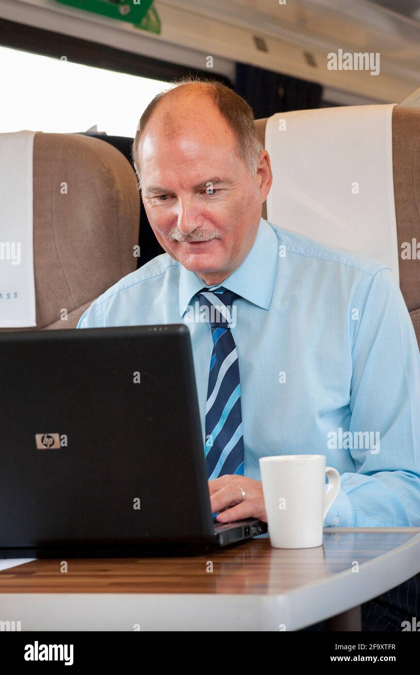 Uomo d'affari che lavora su un computer portatile mentre viaggia su un treno nel Regno Unito. Foto Stock