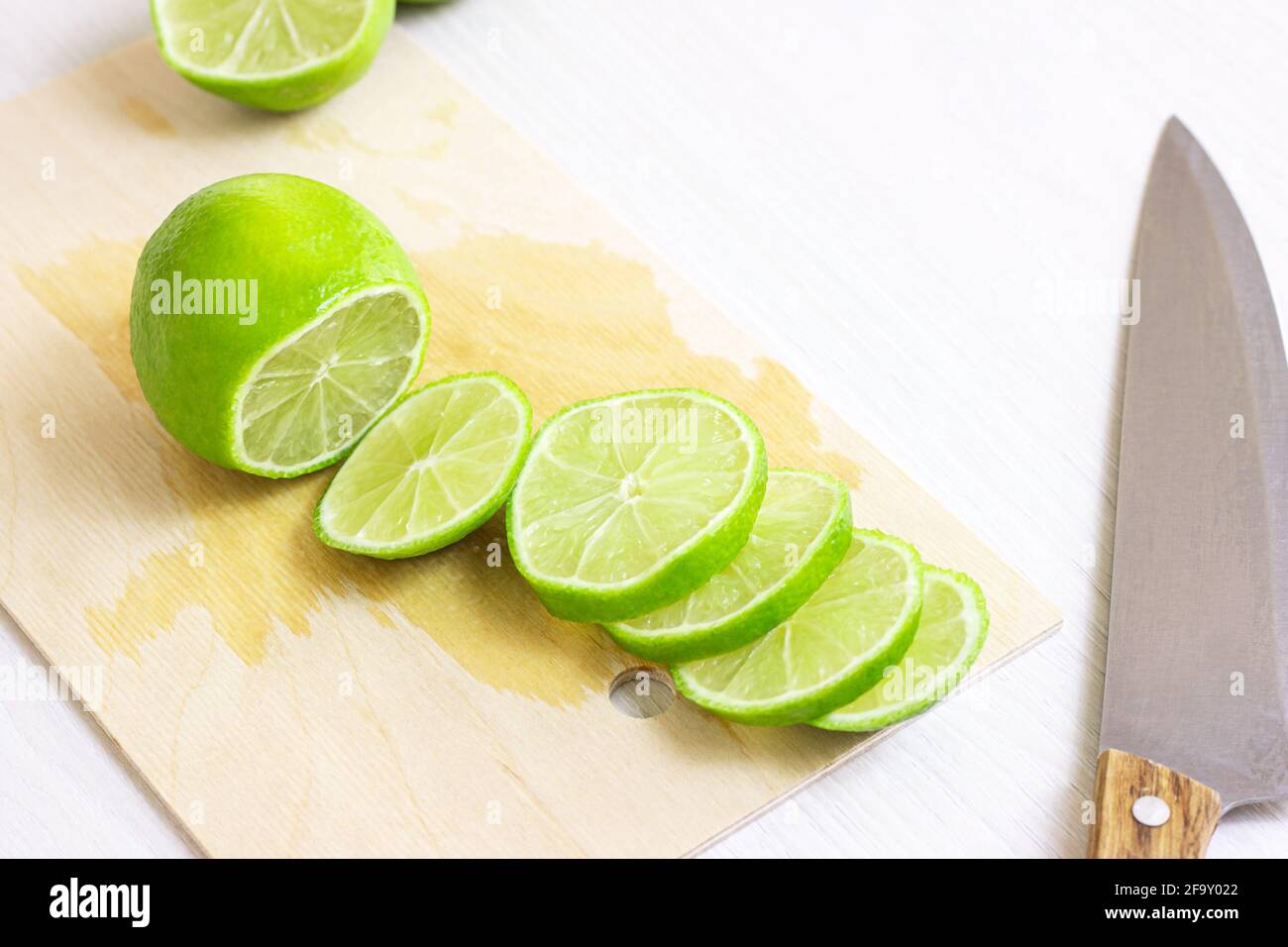 Tiglio fresco verde acido tagliato con il coltello su tagliere di legno chiaro in cucina. Foto Stock