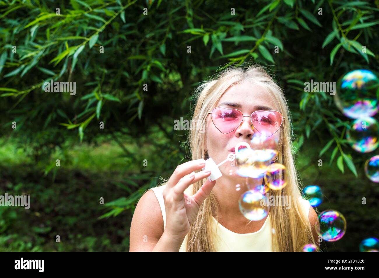 La giovane donna soffia bolle di sapone per strada. Primo piano verticale. Concetto di felicità ed emozioni positive Foto Stock