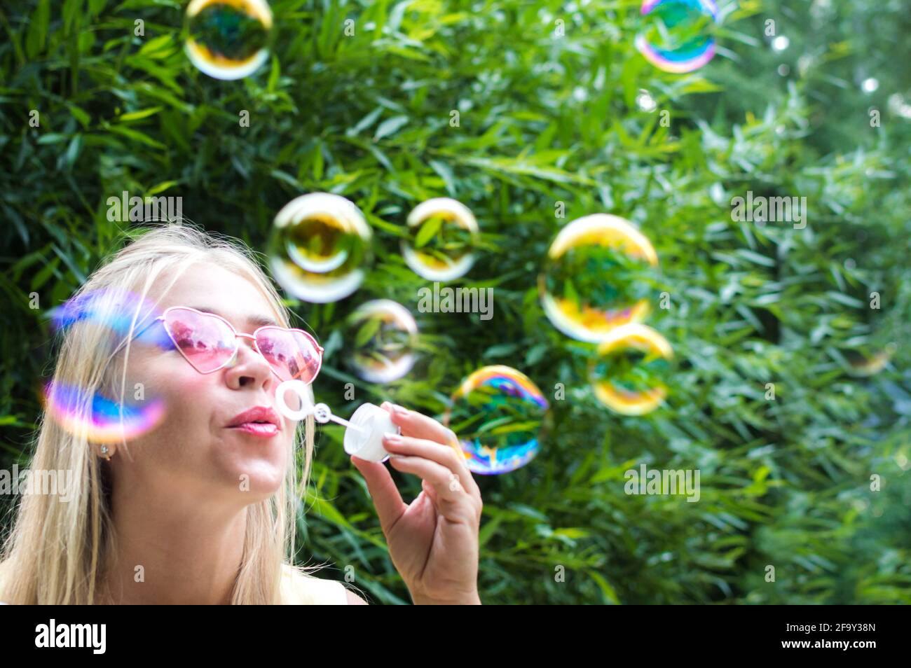 La giovane donna soffia bolle di sapone per strada. Primo piano verticale. Concetto di felicità ed emozioni positive Foto Stock