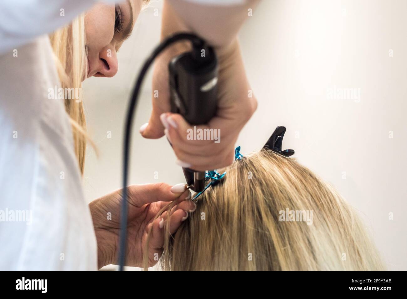 il padrone fa le estensioni dei capelli ad una donna. Primo piano del processo. Foto Stock