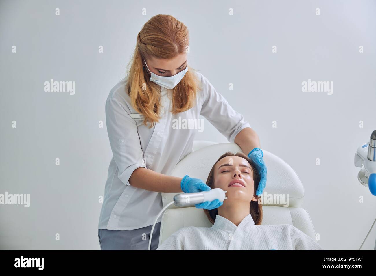 Giovane adorabile donna decapitata in accappatoio bianco ricevendo professionale anti procedura di invecchiamento della pelle in clinica di bellezza Foto Stock