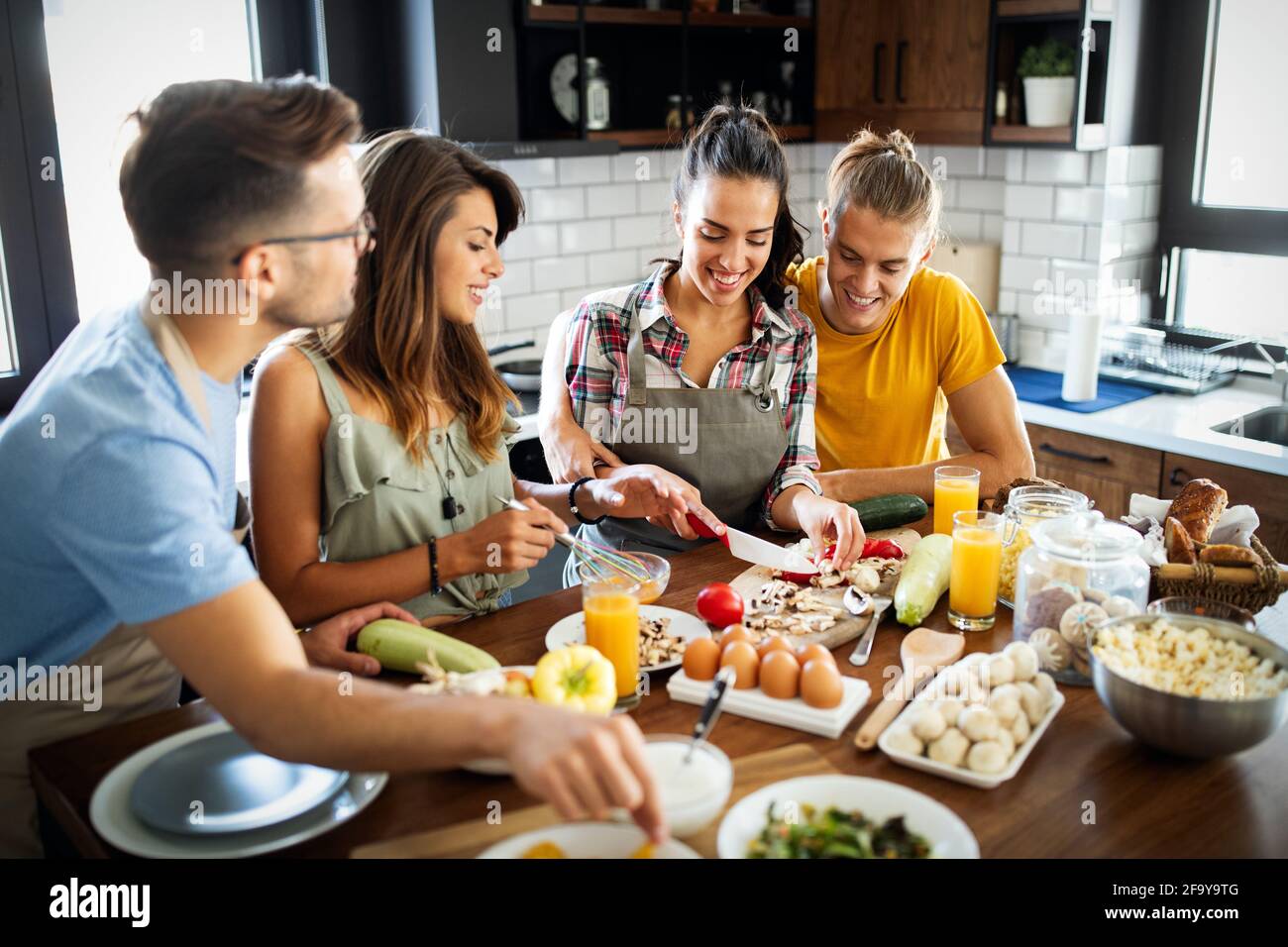 Gruppo di amici felici che ridono e parlano mentre preparano i pasti in cucina Foto Stock