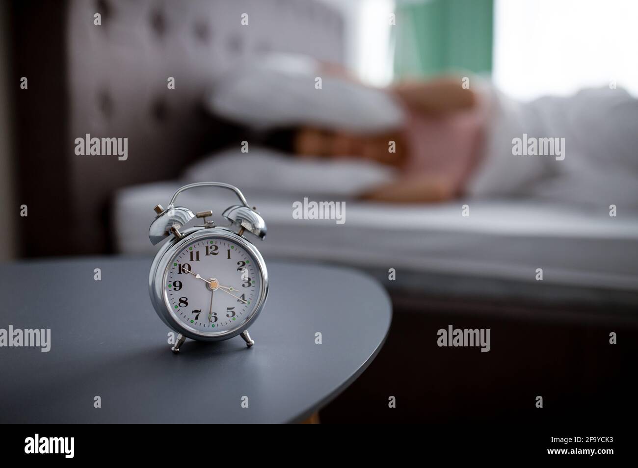 Sveglia sul comodino e vista offuscata della giovane donna che non vuole  svegliarsi, coprendo le orecchie con cuscino nel letto Foto stock - Alamy