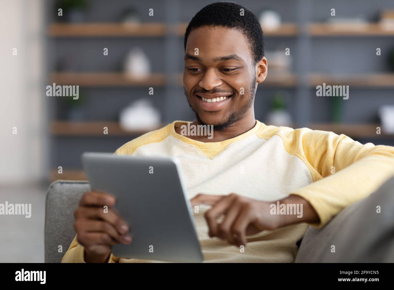 Uomo nero positivo reclinato sul divano, utilizzando tablet digitale, closeup Foto Stock