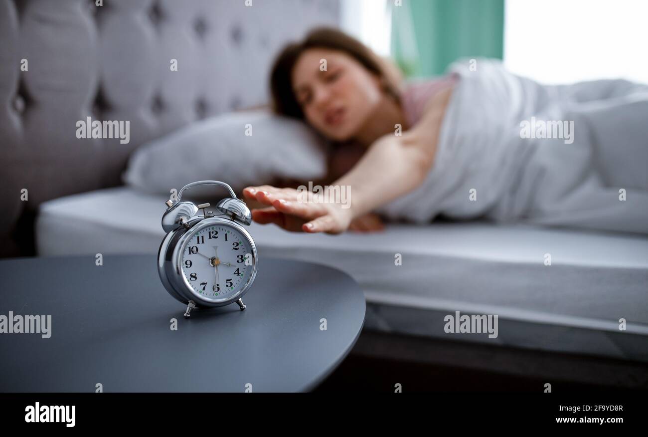Giovane donna che si sveglia e si spegne sveglia, sdraiata a letto al mattino, non disposta ad andare al lavoro, copia spazio Foto Stock