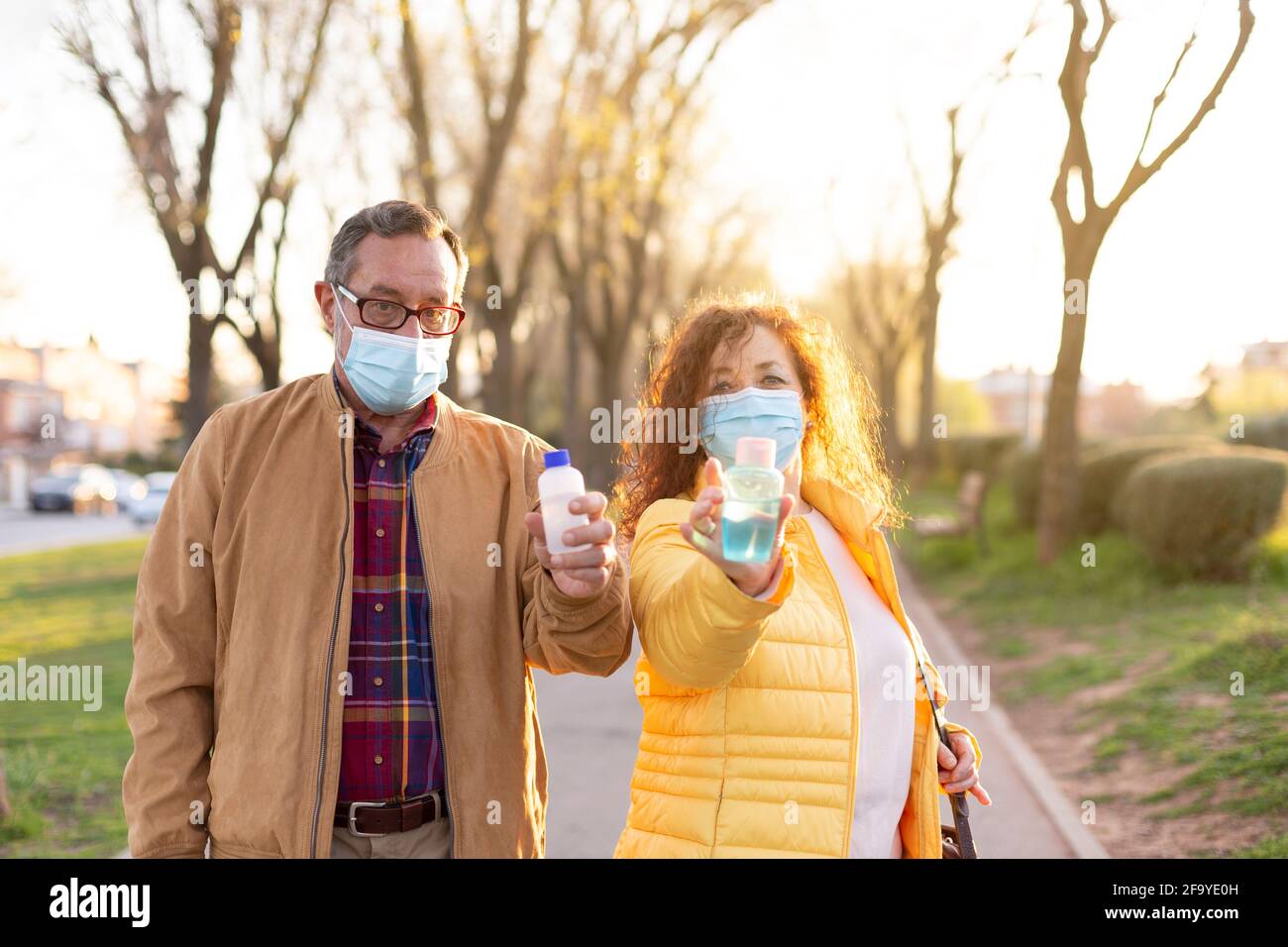 La coppia più anziana indossa una maschera protettiva che mostra gel idroalcolico per la pulizia delle mani durante il tempo di percorrenza. Concetto di cura e misure per proteggere o Foto Stock