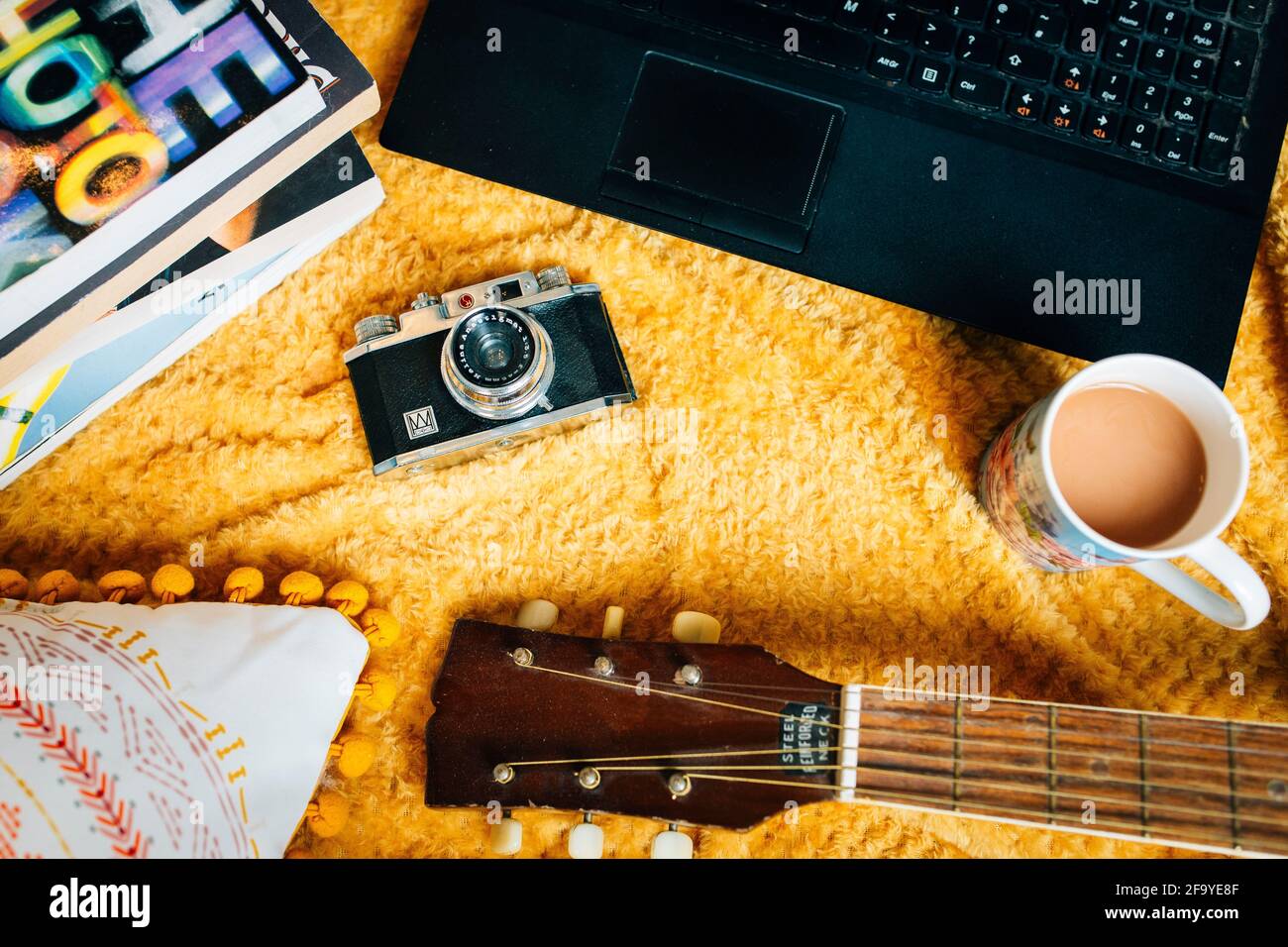 Still life, disteso piatto di una casa accogliente scena. Una coperta sul pavimento con una chitarra, una macchina fotografica di film d'epoca, libri e tè. Stile di vita creativo per freelance Foto Stock