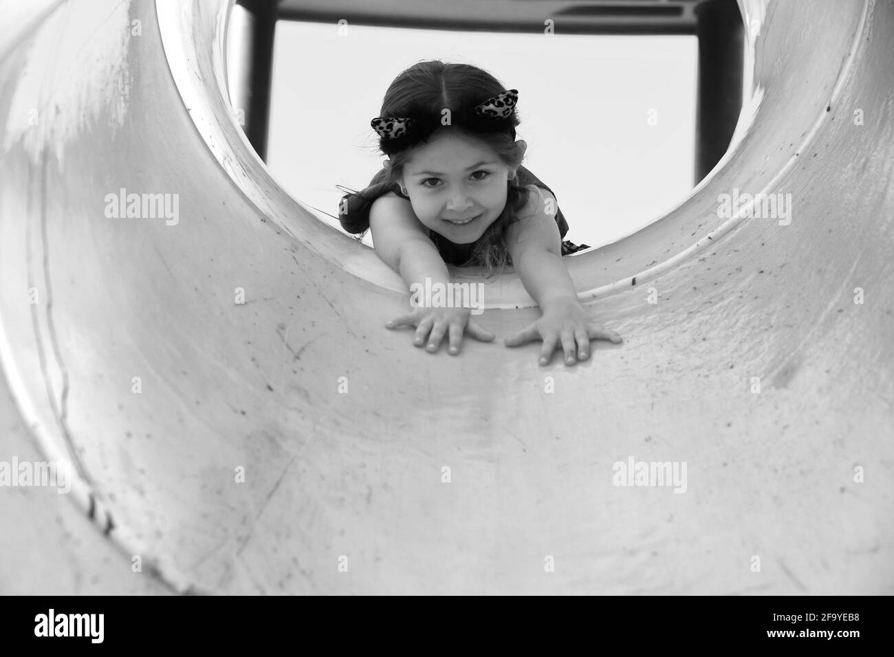 giovane ragazza che gioca nel tubo sul parco giochi indossando orecchie di gatto foto in bianco e nero Foto Stock