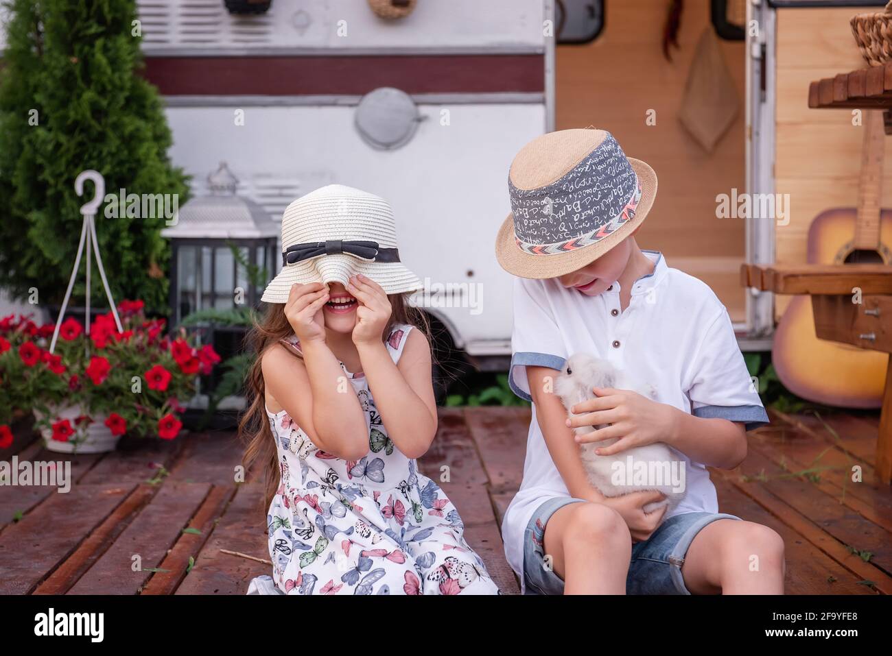 Ragazzo e ragazza si divertono a casa camion rimorchio su pavimento di legno, tenendo morbido coniglio coniglietto nelle loro mani. Fratello e sorella ridono, lanciano la paglia h. Foto Stock