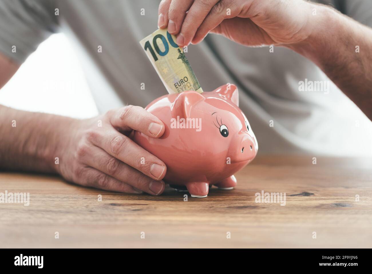 primo piano di uomo che mette soldi in banca piggy a tavola di legno, soldi di risparmio o concetto finanziario Foto Stock