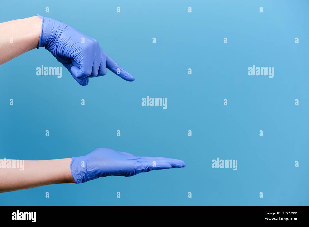 inriconoscibile giovane uomo che apre e punta sul palmo sullo spazio di copia da parte, indossa guanti di protezione medica, isolato sulla parete blu di sfondo dello studio Foto Stock
