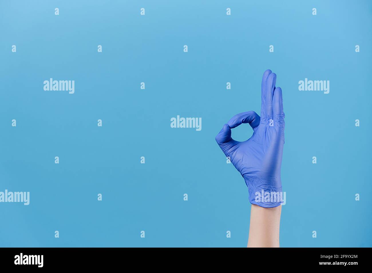 Primo piano della mano maschile in guanti di protezione medica dimostra ok segno, isolato in sfondo blu studio con spazio di copia, esprime la celebrazione Foto Stock