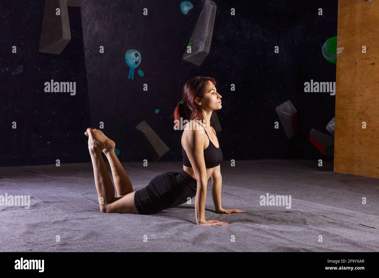 Giovane donna atletica che pratica yoga in palestra interna arrampicata, riscaldamento prima di bouldering Foto Stock