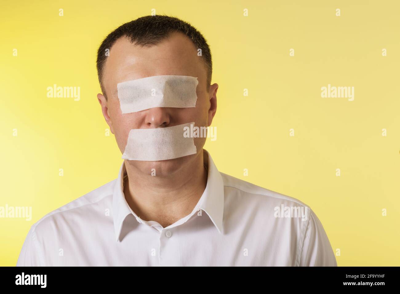 Un uomo con gli occhi e la bocca sigillati con un nastro di pittura su uno sfondo giallo, il concetto non ha paura di dire la verità. Foto Stock