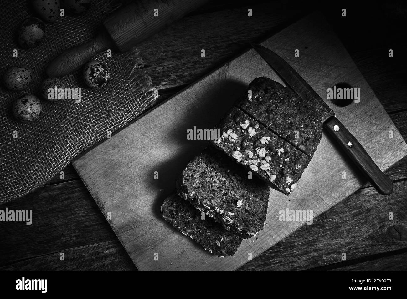 Pane di pane di cereali a fette e uova di quaglia su un vecchio tavolo di legno vista dall'alto, in bianco e nero foto Foto Stock