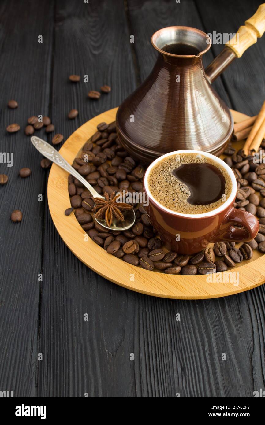 Caffè turco nella tazza marrone e teck sul tagliere su fondo di legno nero. Spazio di copia. Posizione verticale. Foto Stock