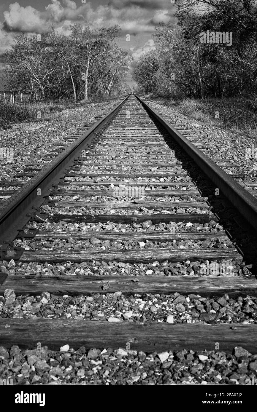 Fotografia in bianco e nero di binari ferroviari che scompaiono nel lontano cielo coperto di nuvole. Trovato sulle strade posteriori del Texas nella regione di collina. Foto Stock