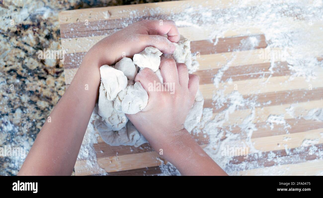 Primo piano delle mani del ragazzo preparazione dell'impasto per la pizza con farina su fondo di legno. Vista dall'alto. Spazio di copia. Foto Stock