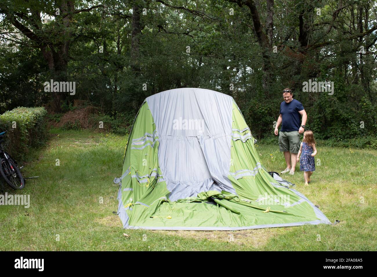 Un padre che ha messo su una grande tenda con l'aiuto delle sue figlie in vacanza in un campeggio. Foto Stock