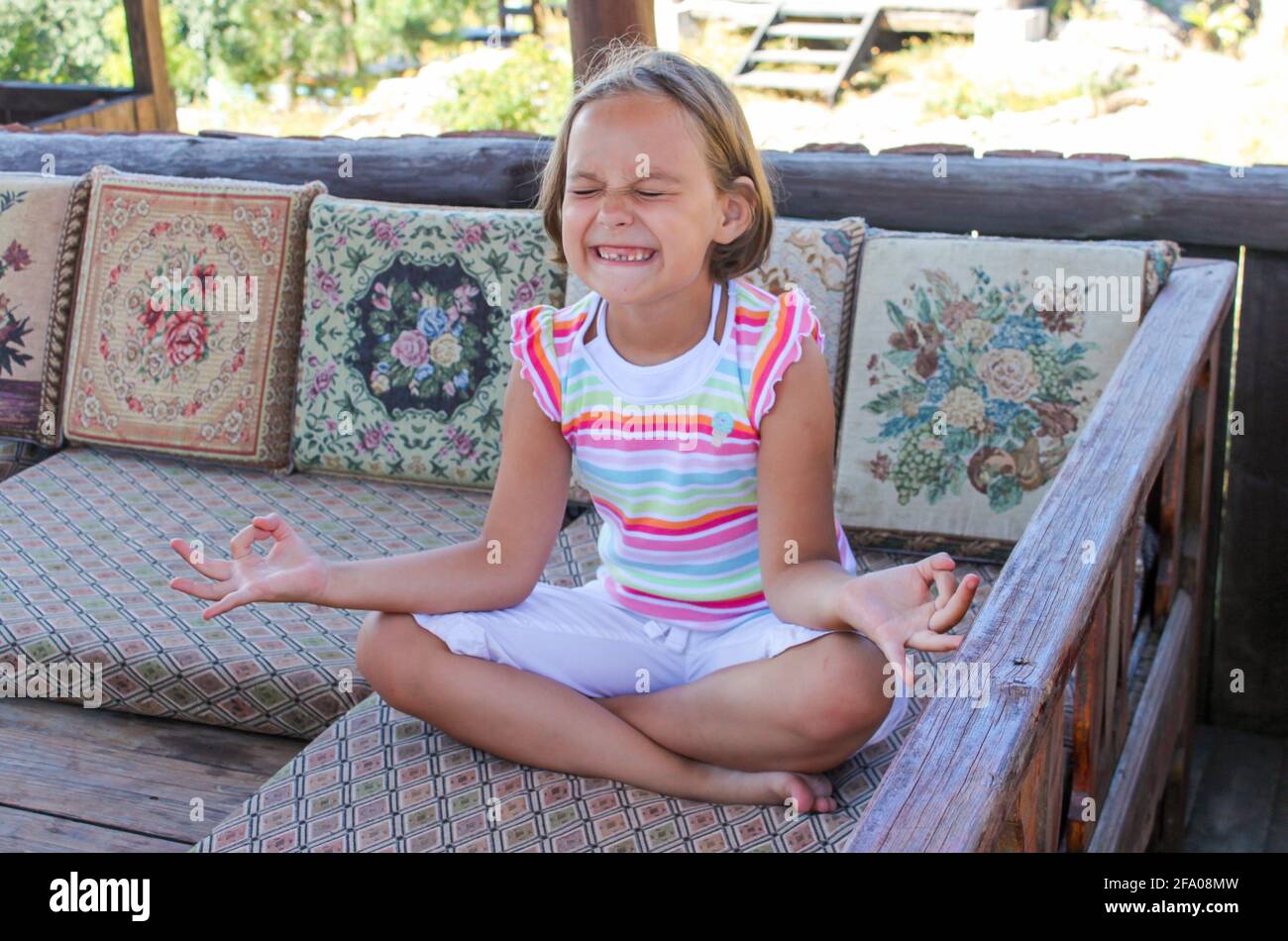 Ragazza divertente senza un dente anteriore nella posizione del loto cerca il suo meglio per meditare. Foto Stock