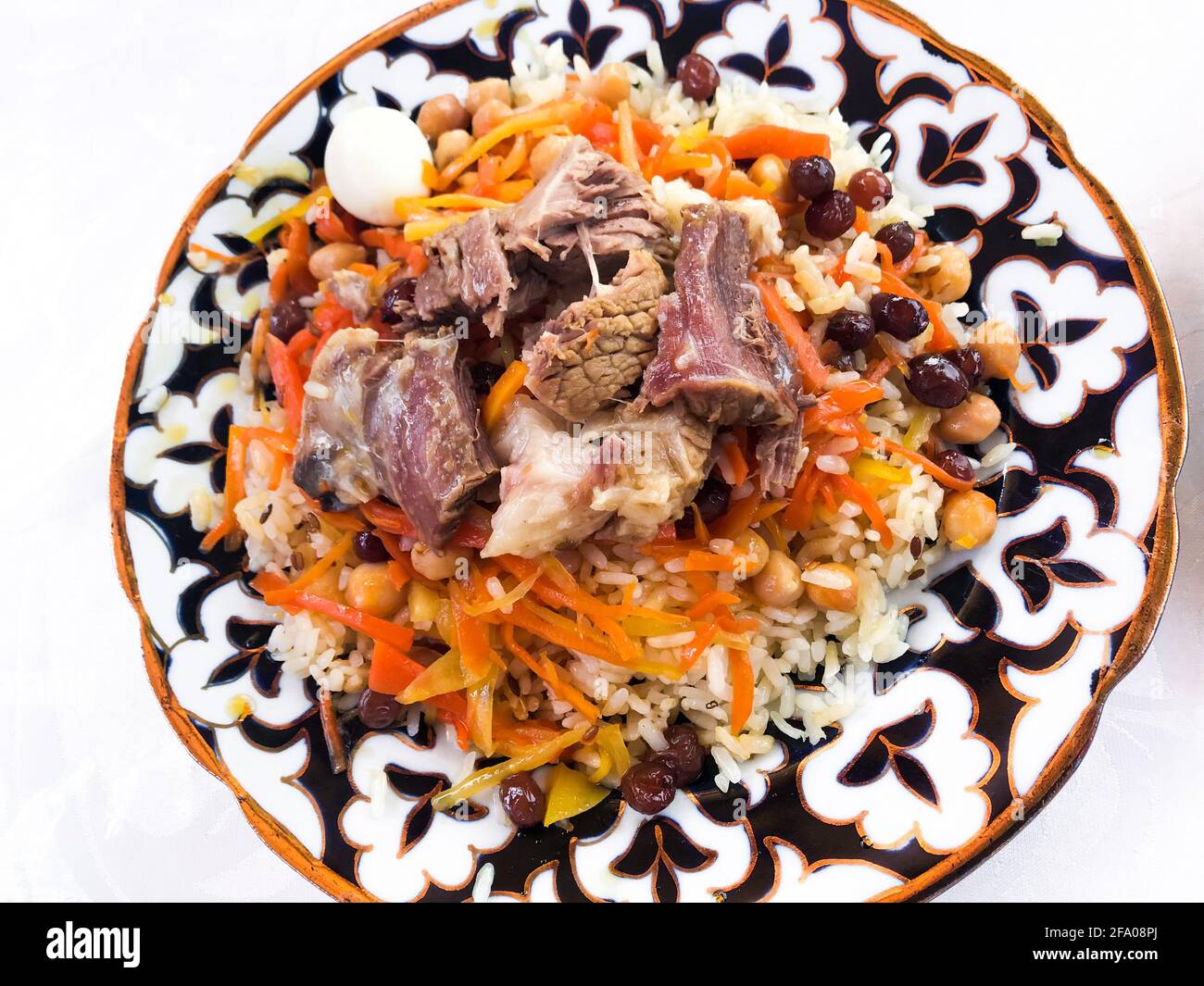 Primo piano di nozze pilaf di riso, cipolle, carote. Con agnello e pollo. Oltre all'uva passa, ai ceci e alle uova. In un piatto con un ornam nazionale uzbeko Foto Stock