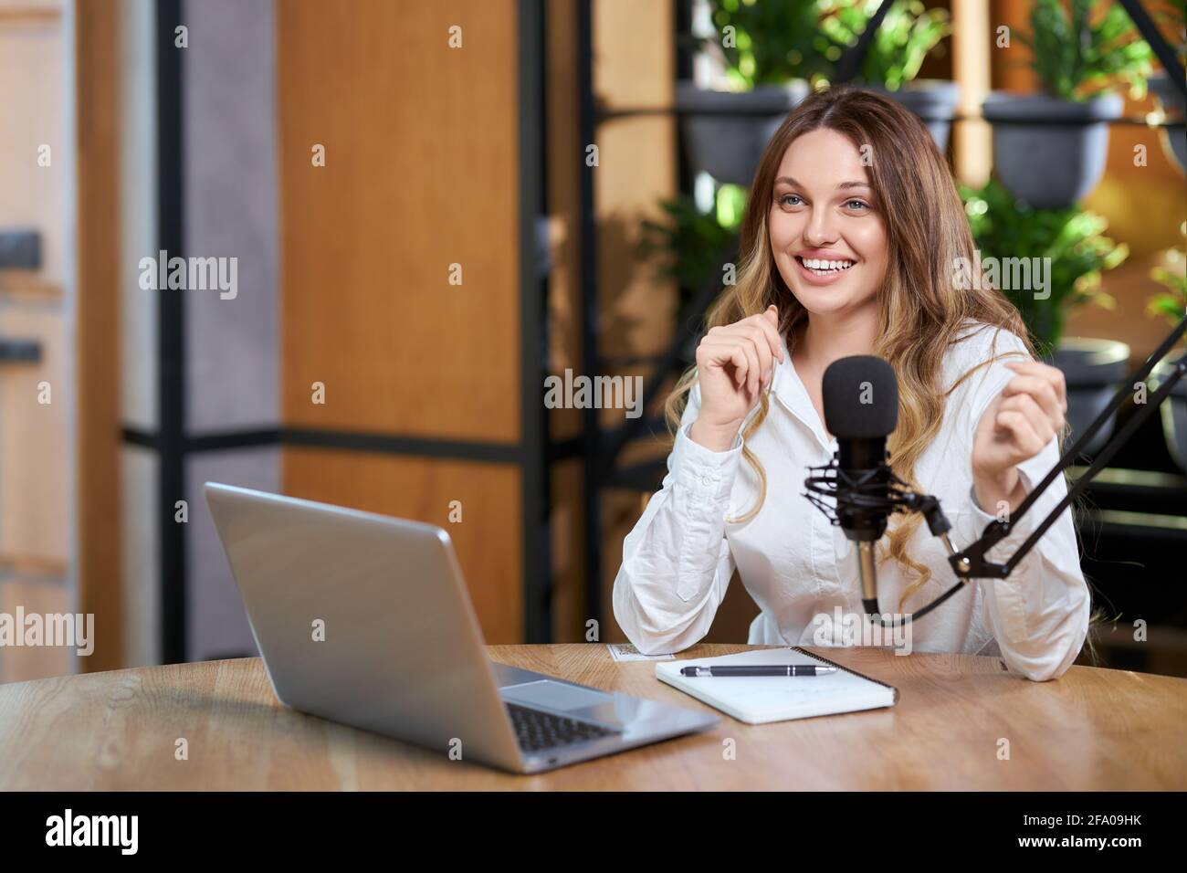 Primo piano ritratto di felice giovane bella donna in camicia bianca che parla di diversi argomenti con i seguaci online per computer portatile. Concetto di intervista o trasmissione in diretta per gli abbonati. Foto Stock