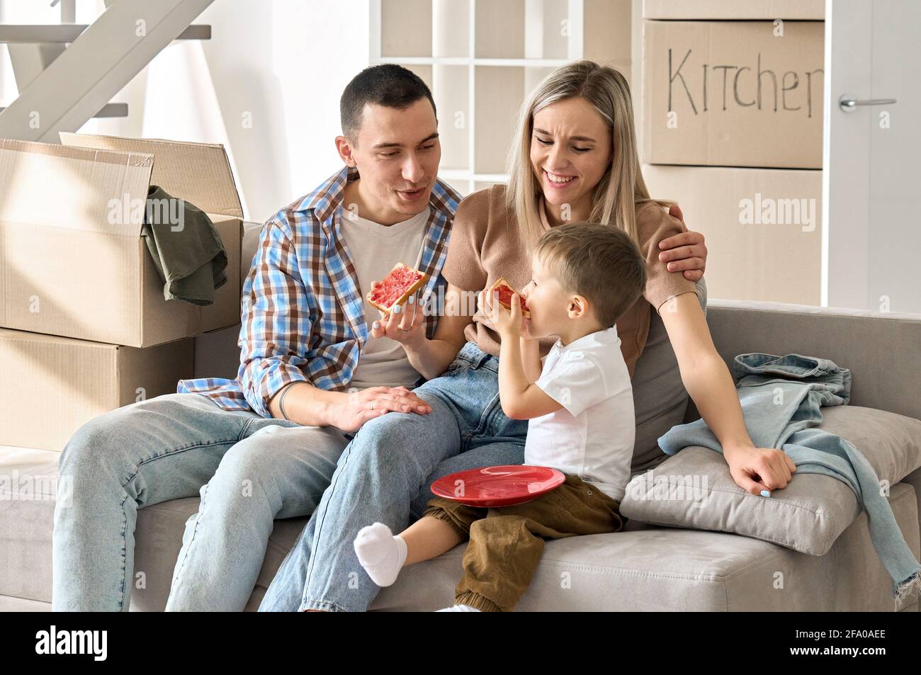 Felice famiglia nuovi inquilini con bambino seduto sul divano a casa nuova a giorno di movimento. Foto Stock