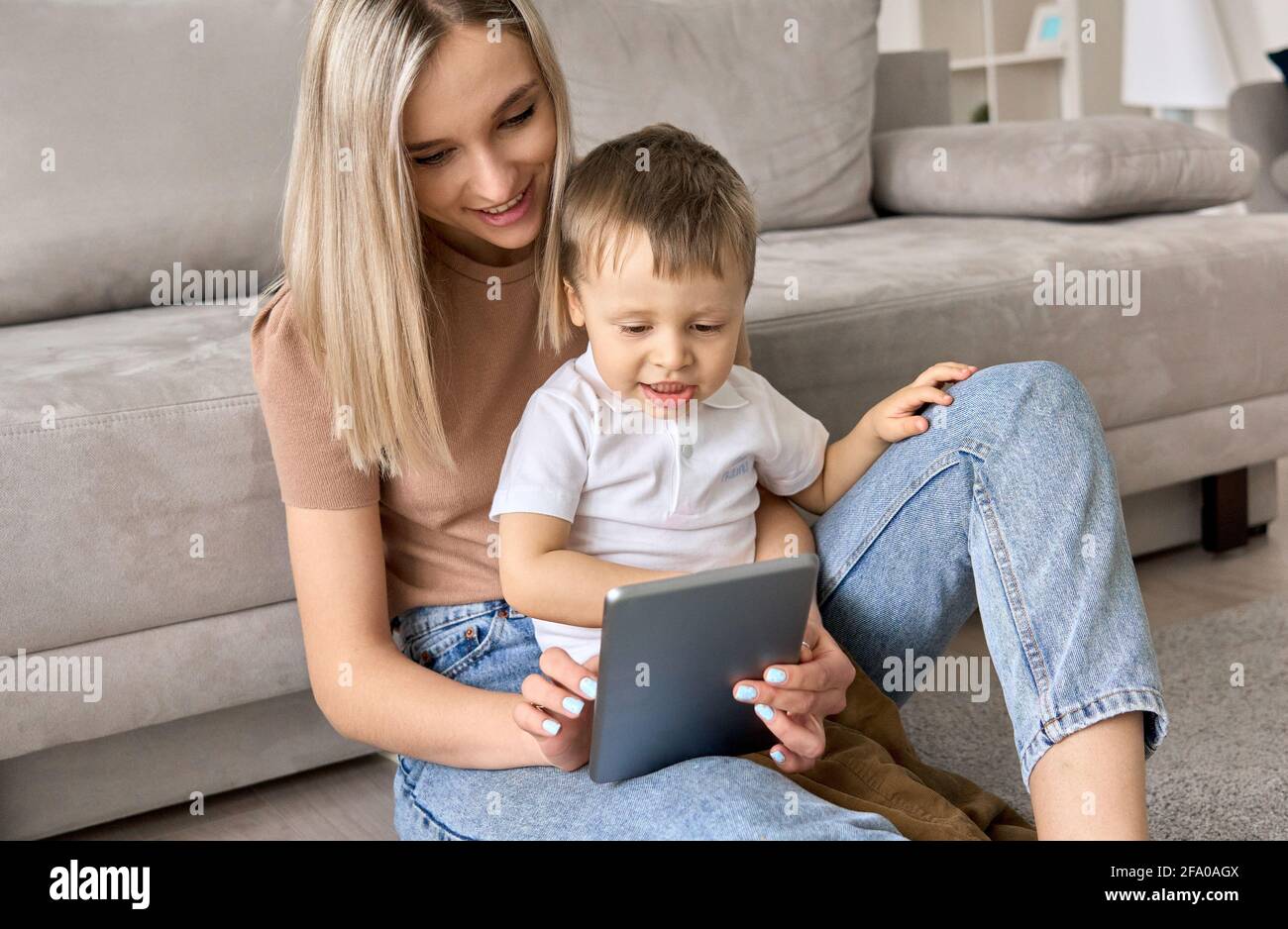 Mamma giovane seduto a casa con un bambino che guarda i film sul tablet. Foto Stock