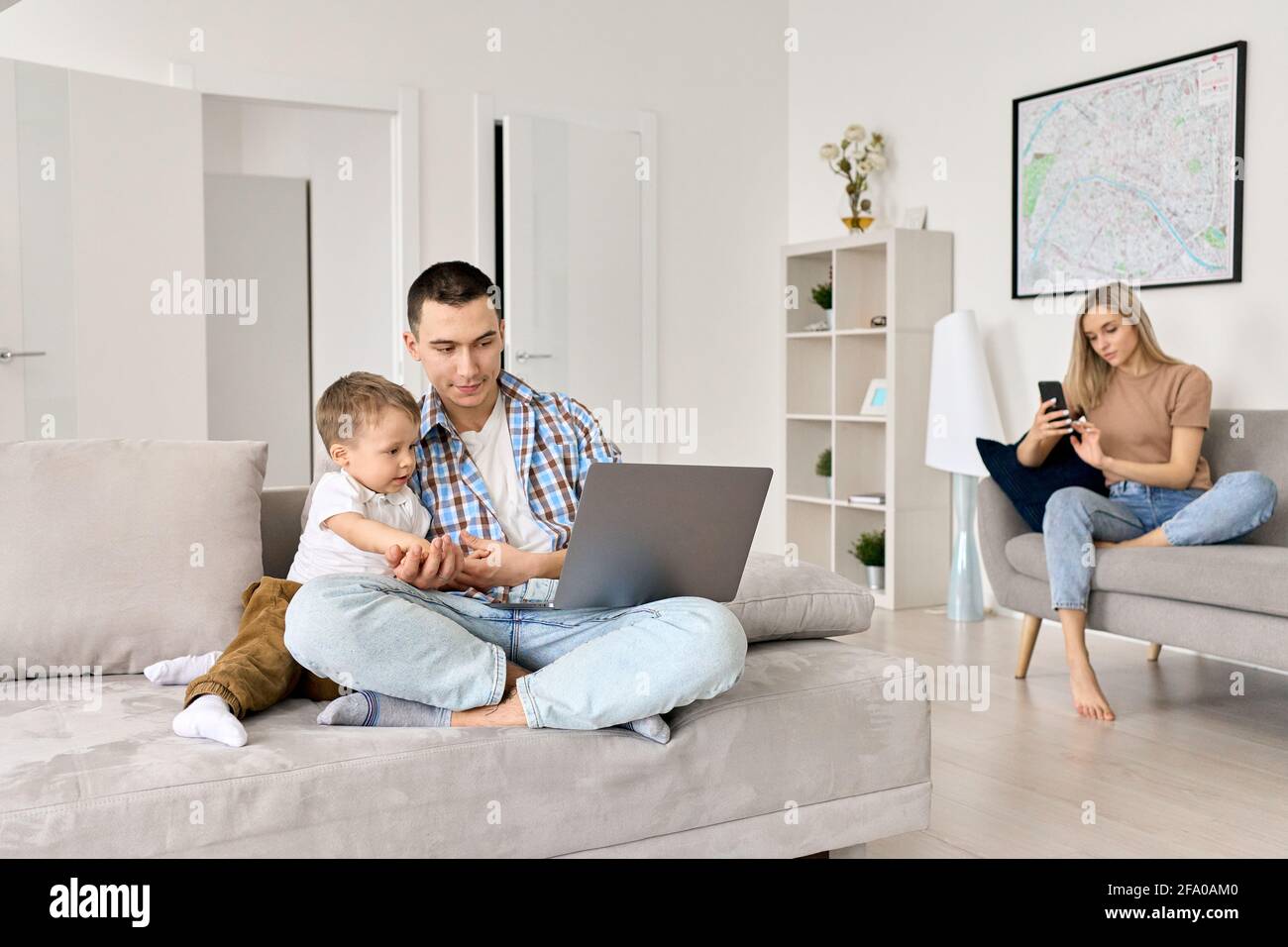 Giovane famiglia con bambino a casa che guarda le lezioni online, navigando sui social media. Foto Stock