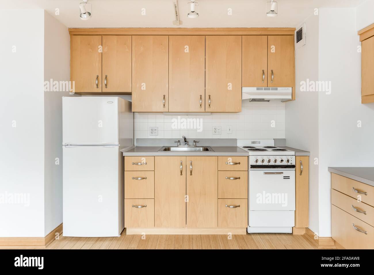 Una cucina d'acero in un appartamento di città vuoto con elettrodomestici bianchi, ripiani in granito, molti armadi per lo stoccaggio, e pavimenti in legno duro. Foto Stock