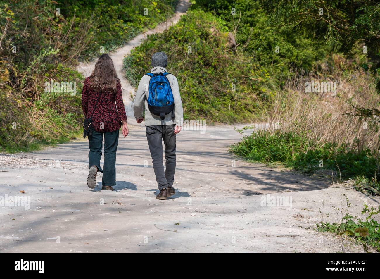 Una coppia maschile e femminile di persone con uno zaino che cammina lungo un percorso di campagna in primavera nel Sussex occidentale, Inghilterra, Regno Unito. Foto Stock