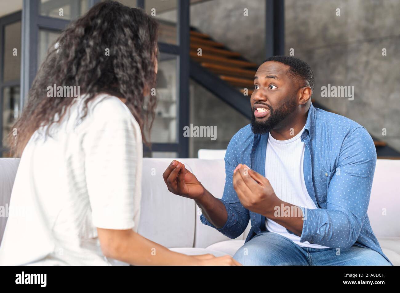 Irritato ragazzo nero urlando contro la donna, arrabbiato ragazzo che sostiene e gesturing con infastidita espressione del viso, afro-americano coppia litigare seduto sul divano a casa Foto Stock