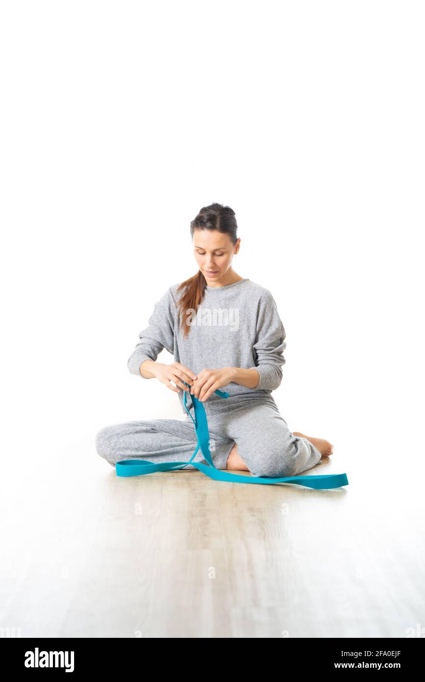 Giovane istruttore di yoga femminile sportivo in uno studio di yoga bianco luminoso, sorridendo allegro mentre si preparano le attrezzature per l'allenamento yoga Foto Stock