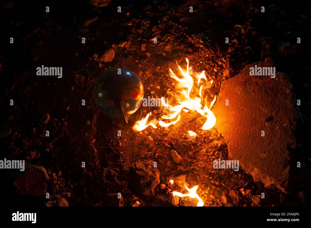 Globe rimanere sul pavimento roccioso vicino al fuoco fiammeggiante Foto Stock