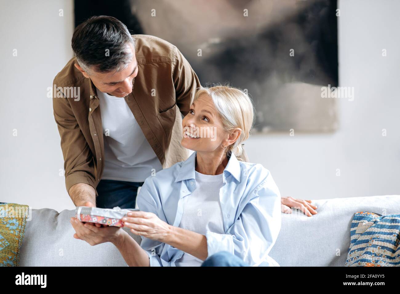 Un marito attento e attento dai capelli grigi dà al suo compagno di anima una piccola scatola bella con un regalo speciale per il loro anniversario di matrimonio, o il suo compleanno. Un marito amorevole dà un dono a sua moglie Foto Stock