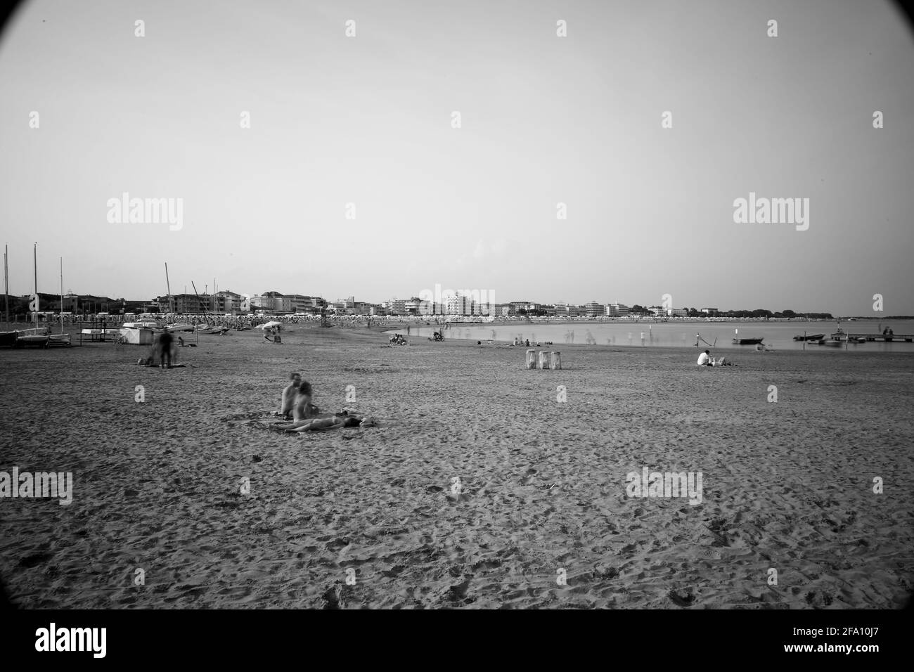 Alta mezzogiorno alla spiaggia di Caorle con persone che si rilassano nell'aria calda e scintillante della spiaggia godendo del sole e del mare Italia Foto Stock